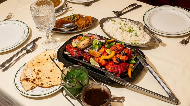 A table set with Indian dishes, including tandoori chicken, rice, curry, naan, and sauces.