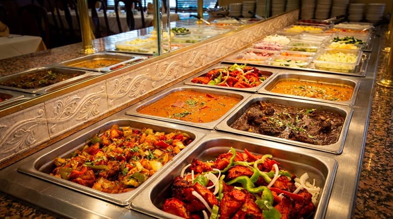 A buffet line with various Indian dishes in metal serving trays, including curries and tandoori chicken.