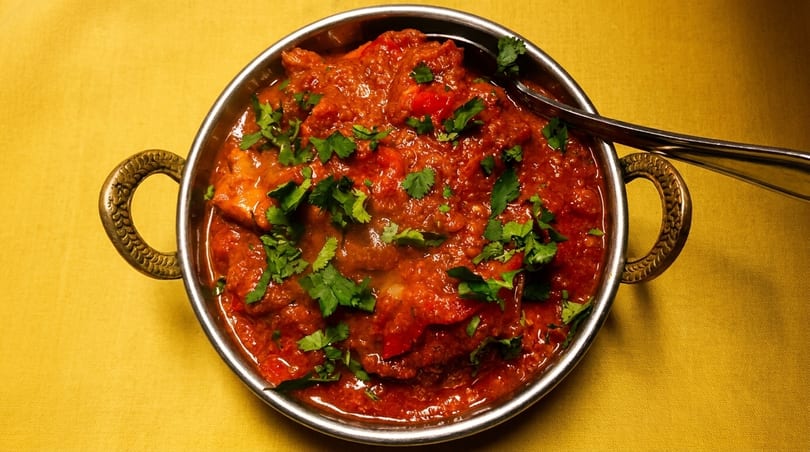 A vibrant red curry, garnished with fresh cilantro, in a metal bowl on a yellow tablecloth.